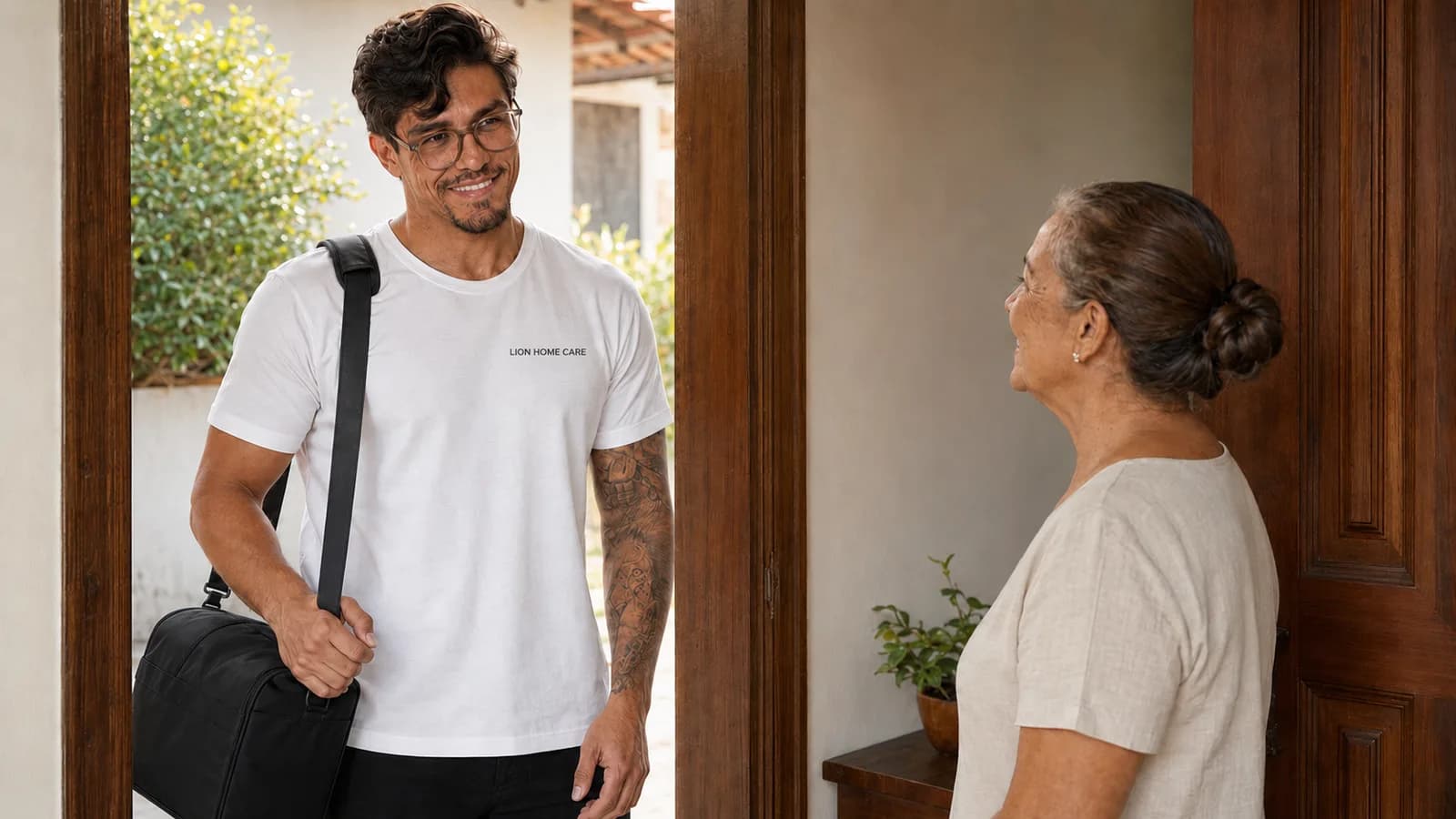 Enfermeiro de home care de camiseta branca lisa sendo recebido na porta de casa por uma senhora idosa, luz da manha