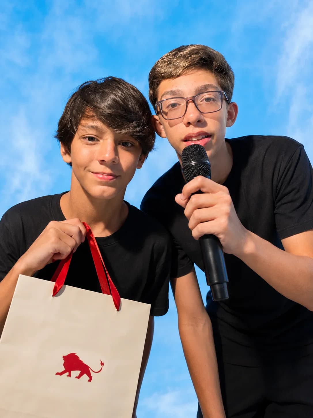 Dois meninos de camiseta preta, um com a sacola de presente da Lion Brazil e outro com microfone