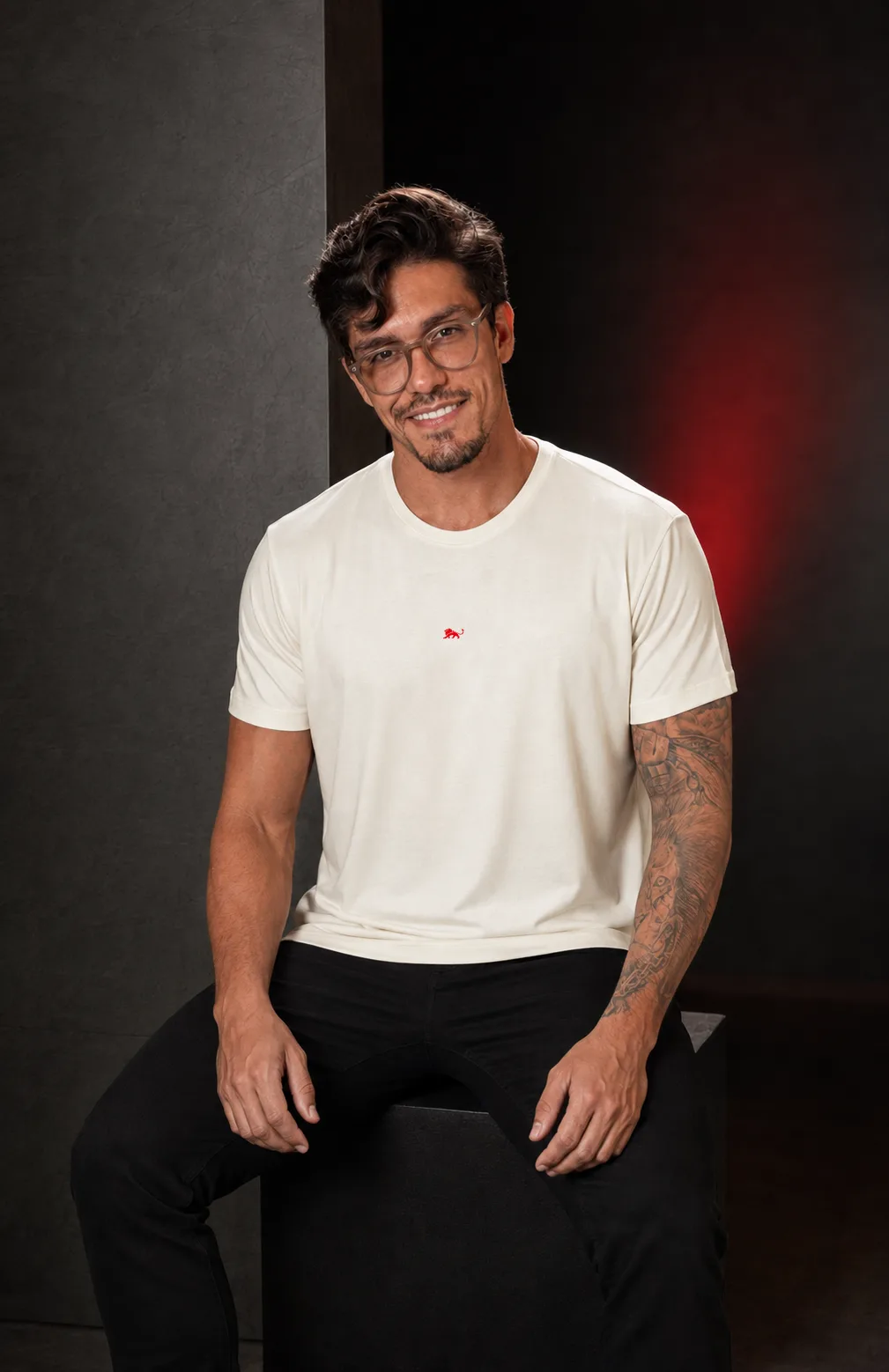 Modelo sentado veste camiseta off-white da Lion Brazil com o leão bordado no peito, ensaio de estúdio · Lion Brazil