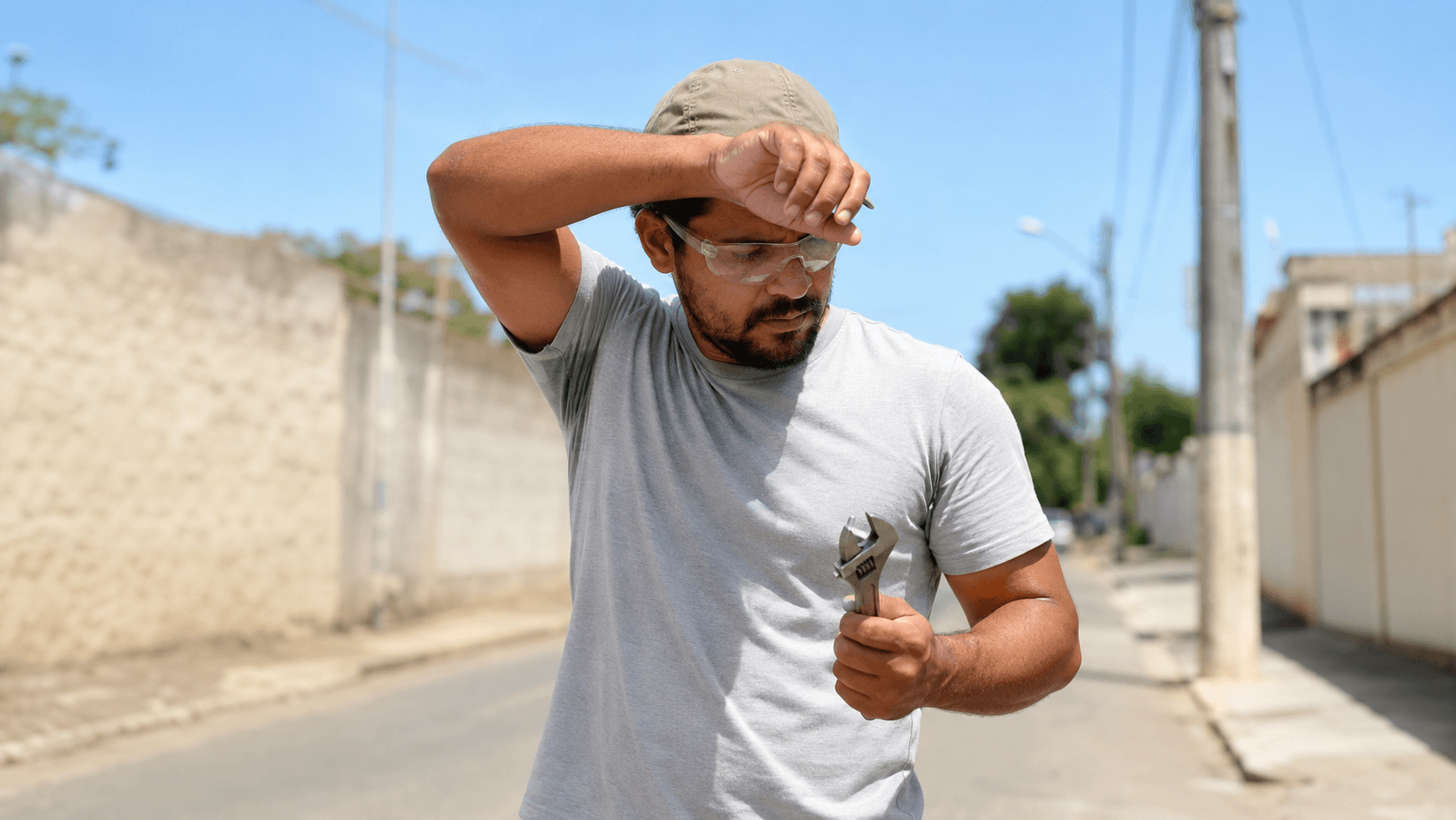 Técnico de camiseta cinza-claro secando a testa durante o trabalho externo sob sol forte