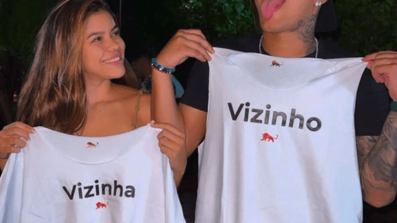 Casal segurando duas camisetas brancas personalizadas com as palavras Vizinha e Vizinho, feitas pela Lion Brazil