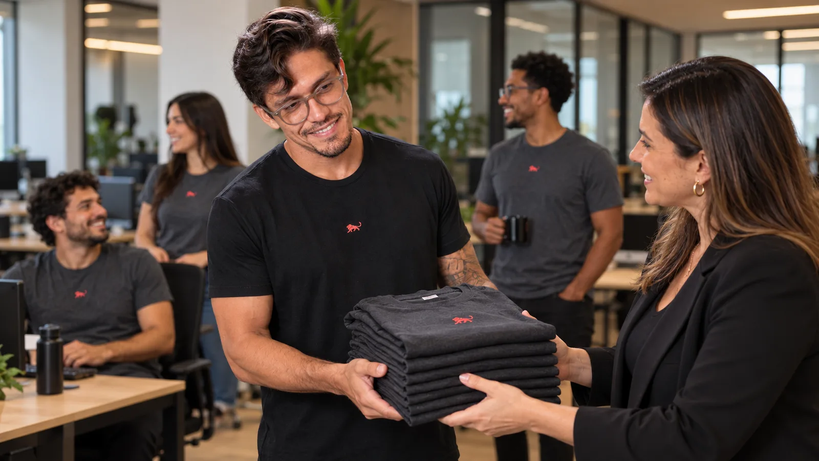 Pedro Costa, fundador da Lion Brazil, entrega uma pilha de camisetas para a gestora de RH enquanto a equipe já trabalha com o uniforme novo.