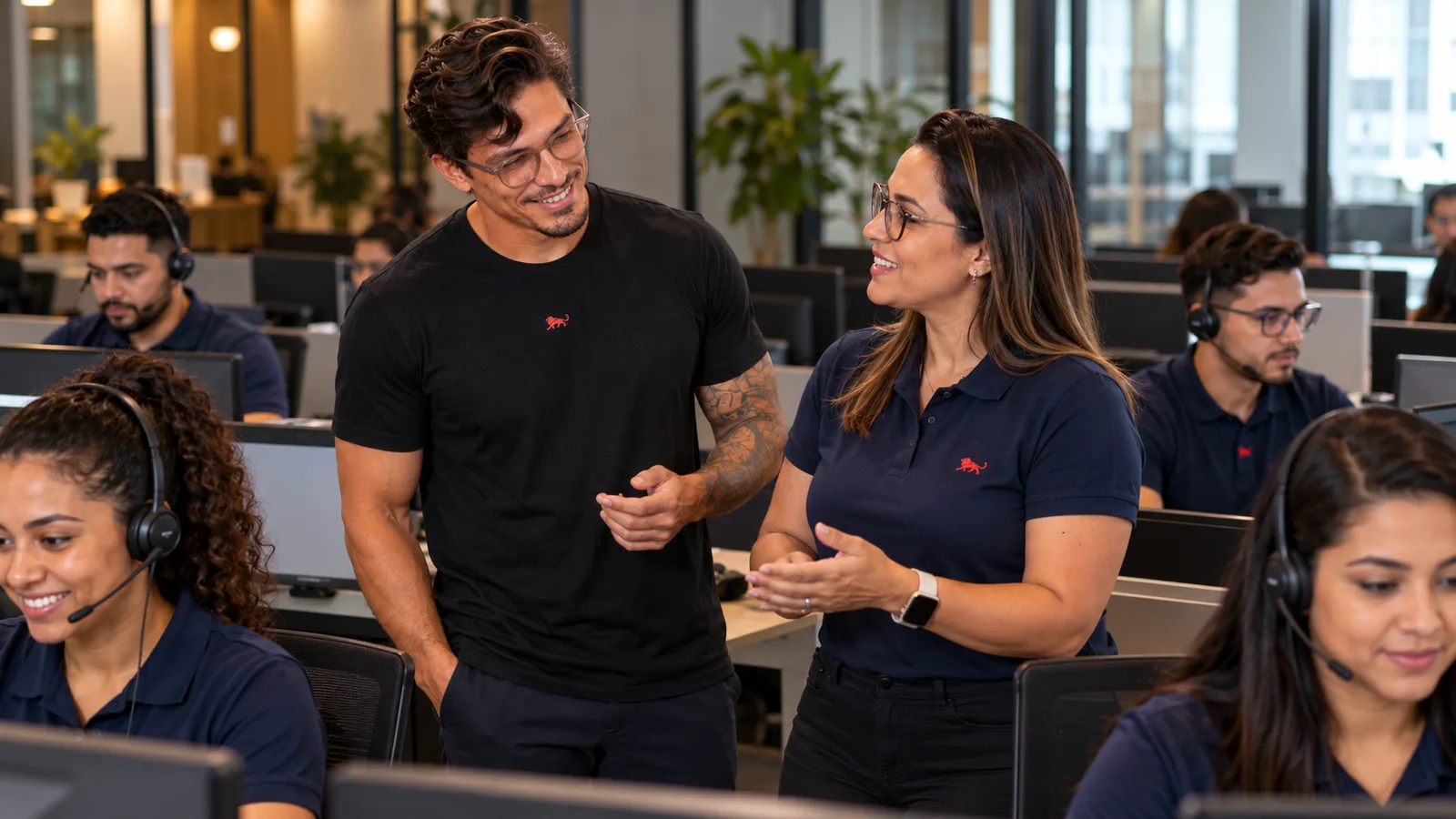 Atendentes de headset e camisa polo azul-marinho com o leão da Lion trabalham nas baias, enquanto Pedro Costa conversa com a supervisora.